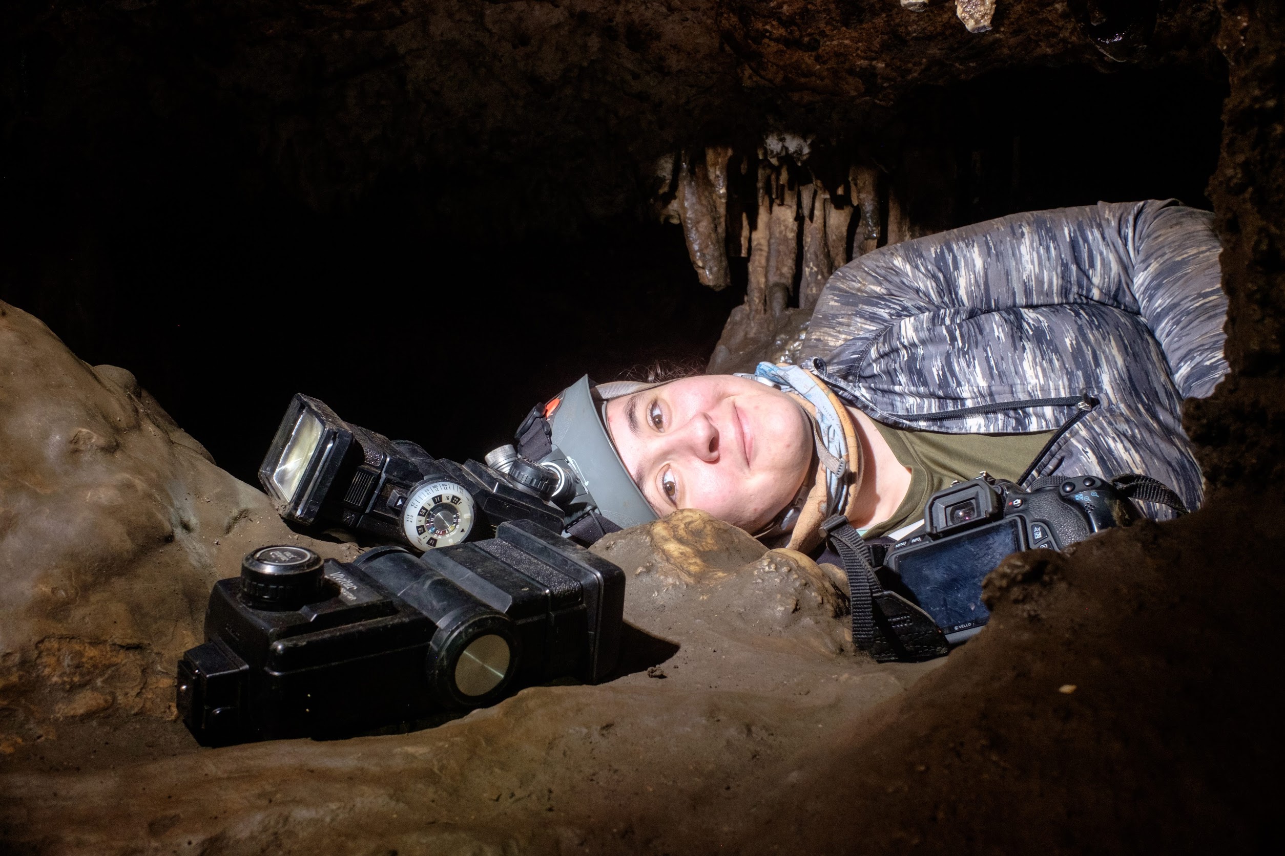Photo of Mara lying in a cave passage with her camera and flashes.